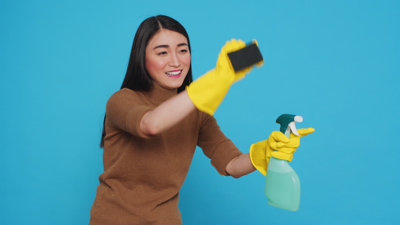 Cheerful housekepper using sponge and professional cleaning detergent while cleaning client home