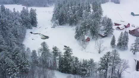 AERIAL-SLIDE-along-a-frozen-river-with-a-small-waterfall,-a-bridge,-and-several-camps-along-its-shore-SLOW-MOTION