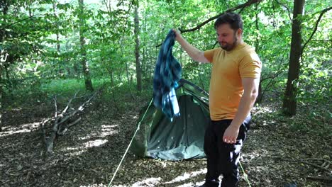 Zeitlupe-Eines-Touristen,-Der-Blätter-Von-Einer-Decke-Vor-Einem-Zelt-Auf-Einem-Waldcampingplatz-Schüttelt