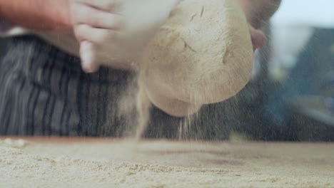 closeup, baker's hands cover the dough with bread flour