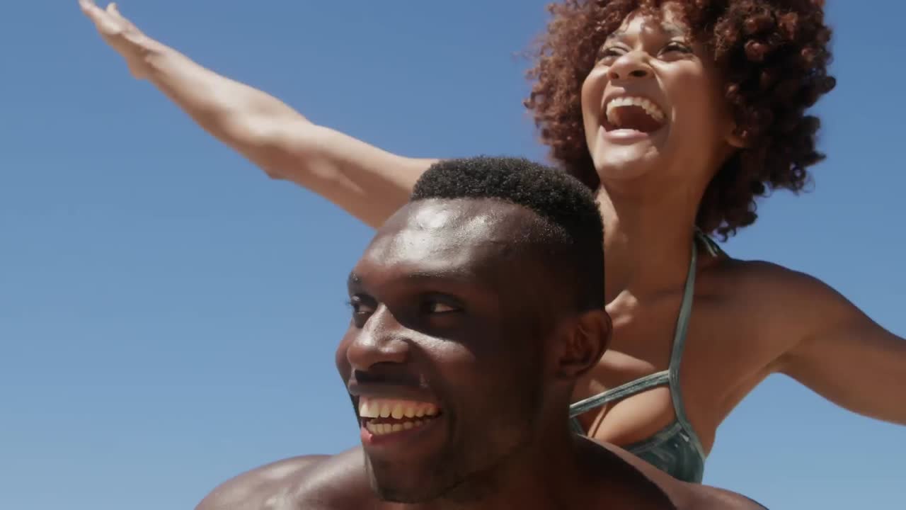 Formes abstraites sur un texte "vibes" au-dessus d'un homme afro-américain portant sa femme sur son dos à la plage