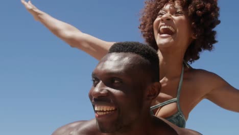 Abstrakte-Formen-über-Vibes-Text-über-Einem-Afroamerikanischen-Mann,-Der-Seiner-Frau-Eine-Huckepackfahrt-Am-Strand-Gibt