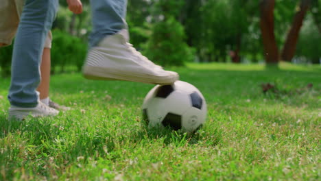 patas humanas desconocidas pateando la pelota en el césped de cerca. padre jugando al fútbol con el hijo.