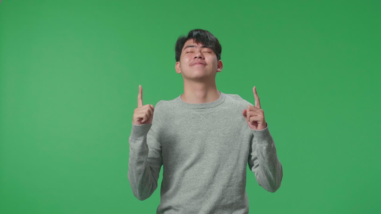 Asian Man Pointing Up While Standing In Front Of Green Screen Background