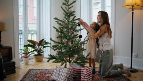 madre y hija alegres decorando el árbol de navidad en casa. madre y hijo poniendo juguetes