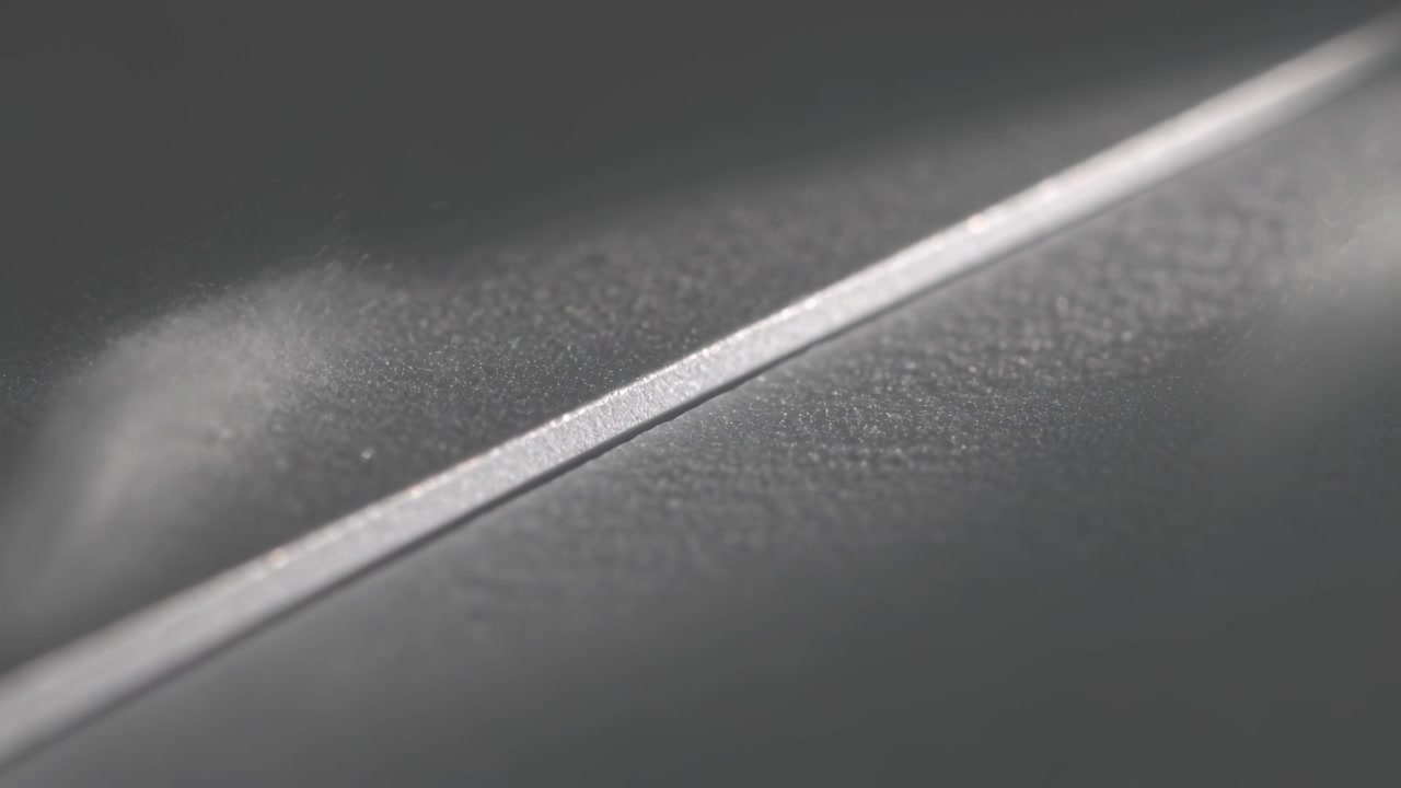 Haze forming left, passing over diagonal metal bevel on studio panel, shifting specular highlight