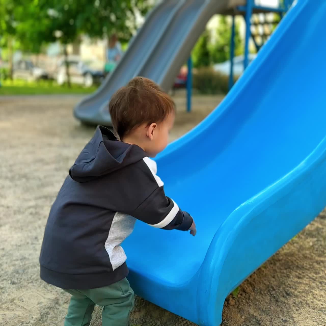 Little boy wants to climb by the slide on the playground. Kid fails every time but doesn't stop trying