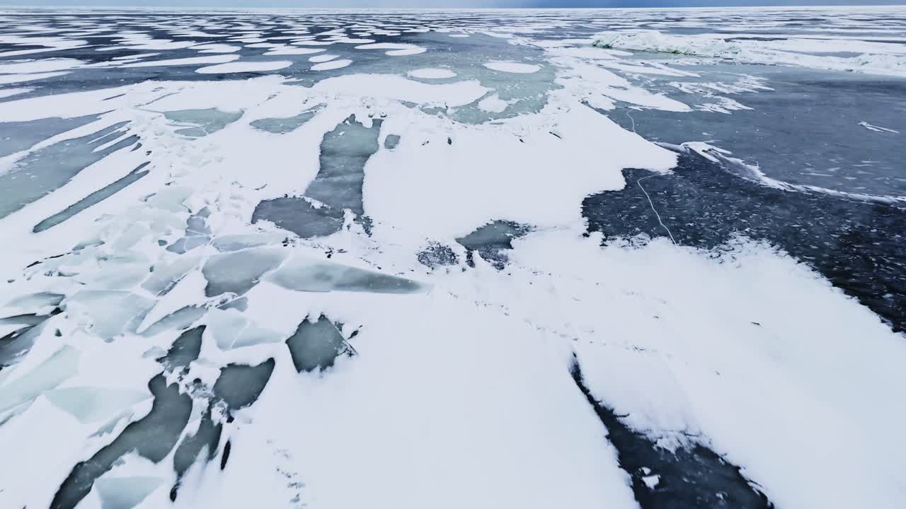 Volo basso di drone su un mare ghiacciato e fratturato con lastre di ghiaccio bianche e fessure d'acqua scure, creando un drammatico pericolo invernale e uno sfondo con texture di disgelo climatico.