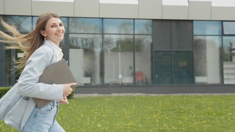 una chica con un traje de negocios con una computadora portátil en las manos corriendo por la calle contra el telón de fondo de un edificio monumental. negocio. chica de negocios atractiva. gente de carrera. mira la cámara