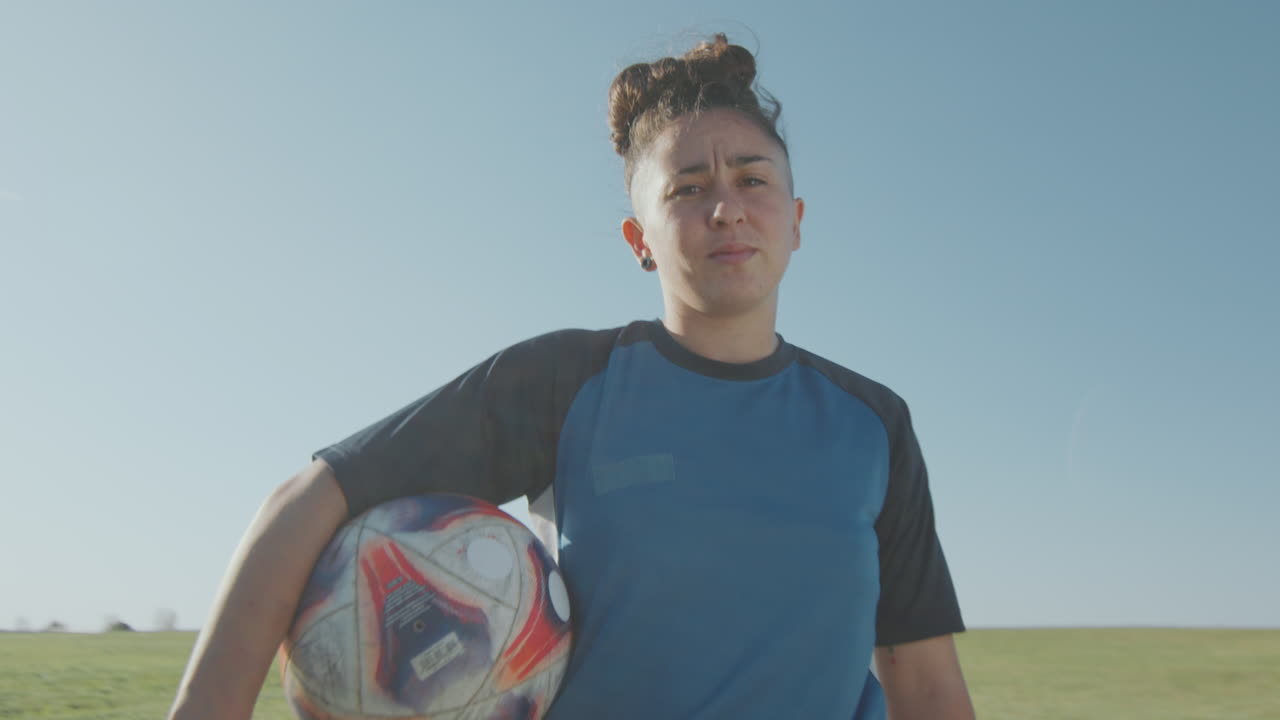 jugadora de fútbol femenina confiada posando en la cámara con la pelota al aire libre