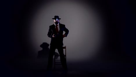 mysterious man in a fedora hat sitting in a spotlight