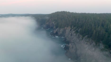 aerial view above water as morning fog approaches rocky maine coastline