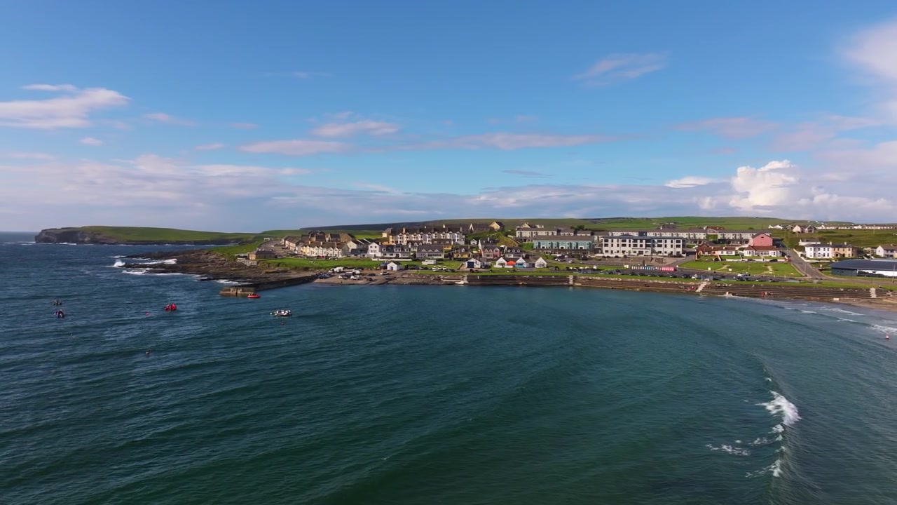 La città costiera di Kilkee, Irlanda, è ripresa con i suoi caratteristici edifici che costeggiano la baia. Dolci onde increspano l'acqua. Adatto per promozioni di viaggio o servizi culturali irlandesi