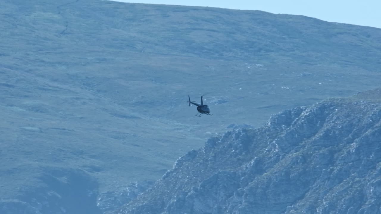 A helicopter flies with a huge mountain in the distance