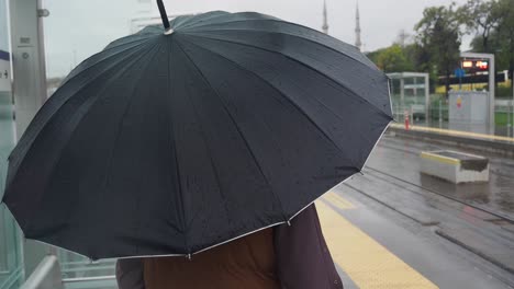 person waiting at a tram stop with an umbrella on a rainy day