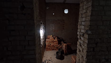 dark room lit with one bulb in the basement. piles of red bricks are on the floor of the premise. construction concept.