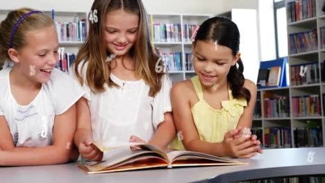 animación de múltiples números y símbolos sobre niñas caucásicas leyendo un libro en la sala de la biblioteca