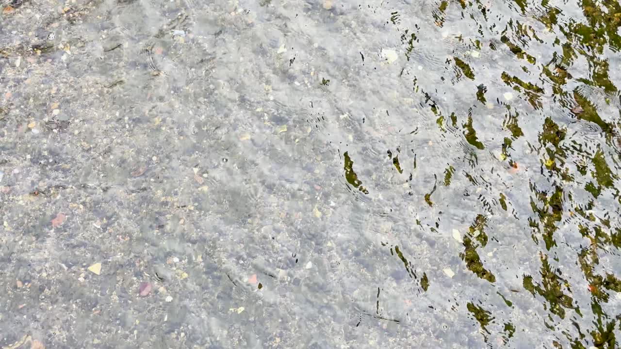 Static high angle shot of shimmering ripples flowing over a shallow pebble river bed