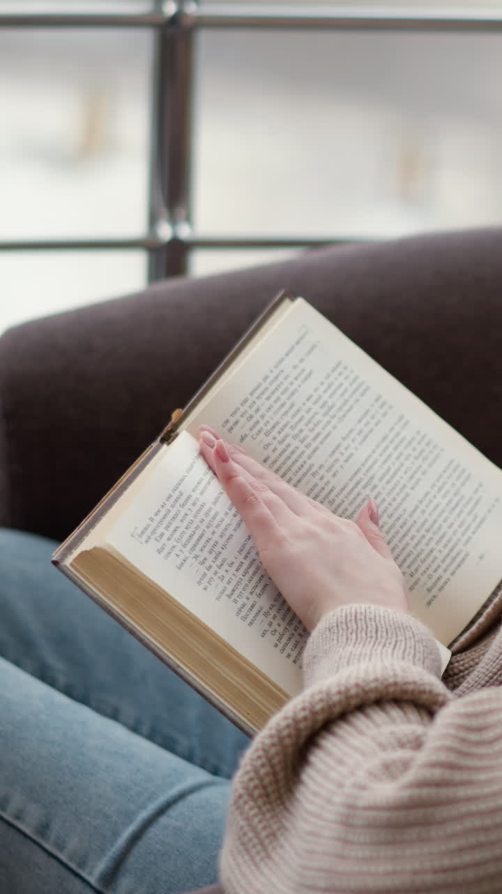 vista lateral de una joven leyendo un libro, con su mano apoyada en las páginas, parece absorta en su lectura, creando una atmósfera pacífica y reflexiva en el entorno acogedor
