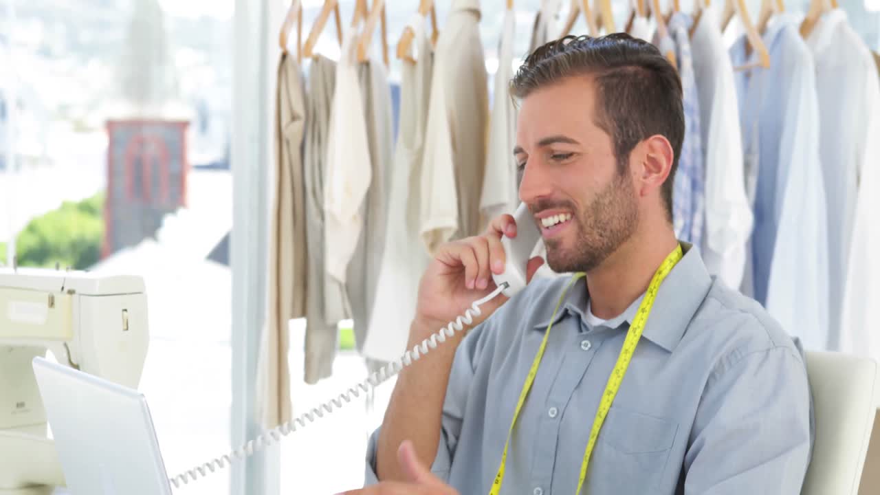 diseñador de moda guapo trabajando en una computadora portátil y contestando el teléfono