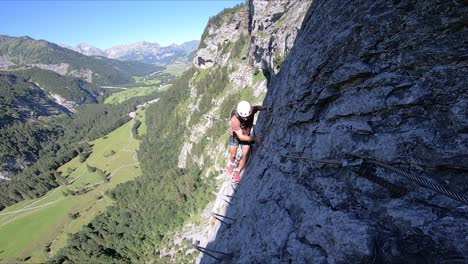 a young man is carefully taking steps on the very small edge of the cliff, walking from the sunshine into the shade during a warm summer day in switzerland