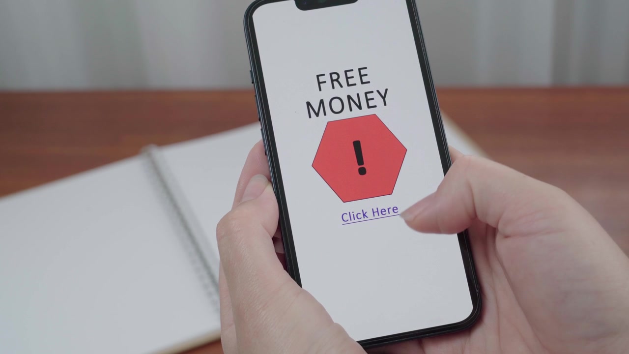 Hånd holder en smartphone med en AI-informationsgrænseflade, der markerer et falsk "Gratis Penge klik her"-tilbud som et potentielt svindelnummer