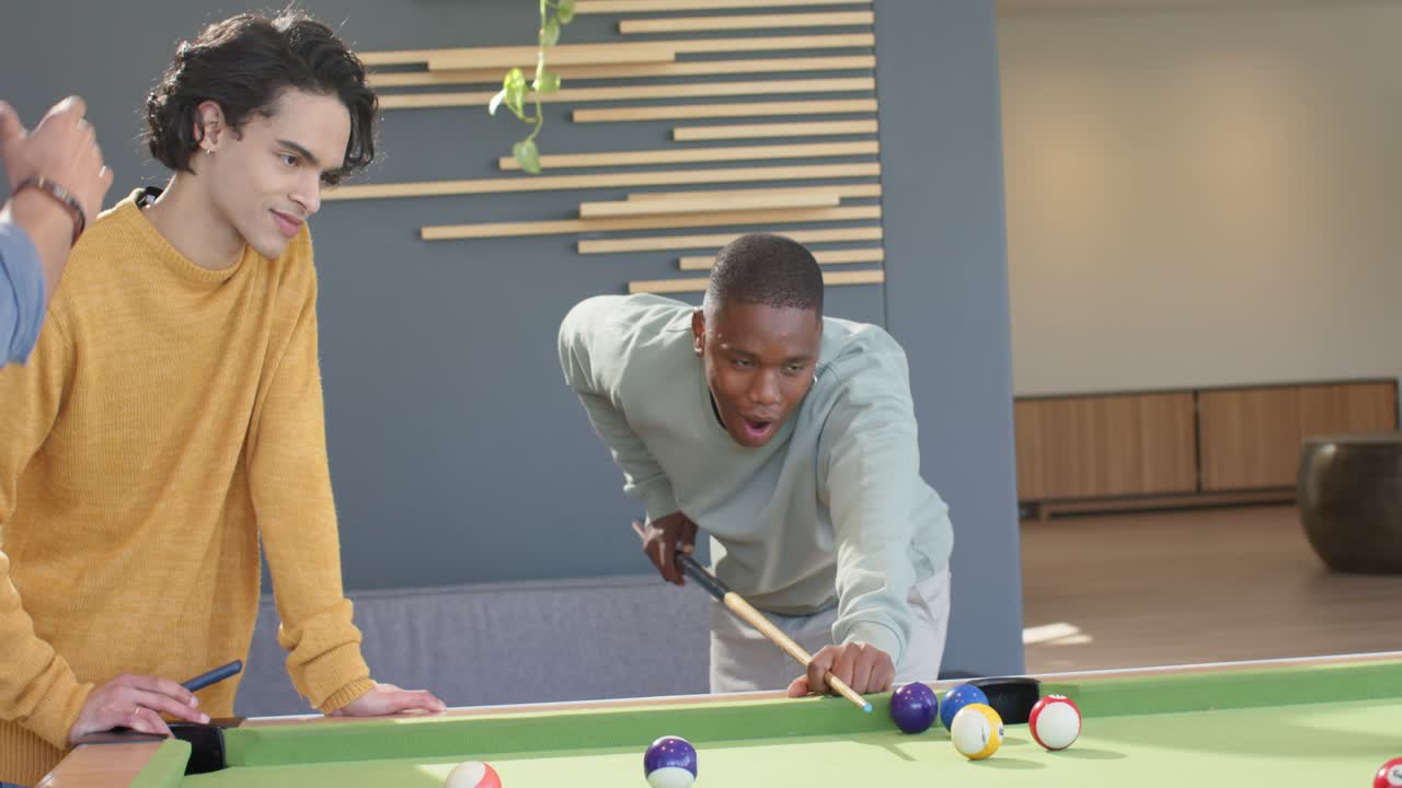 African American man chalking cue, lining shot at pool table in lounge, sinking ball, celebrating