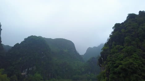 cinematic drone footage of majestic limestone peaks in misty and foggy weather. ricefields in wild jungle in the spring with boat tour canal in tam coc, ninh binh, vietnam