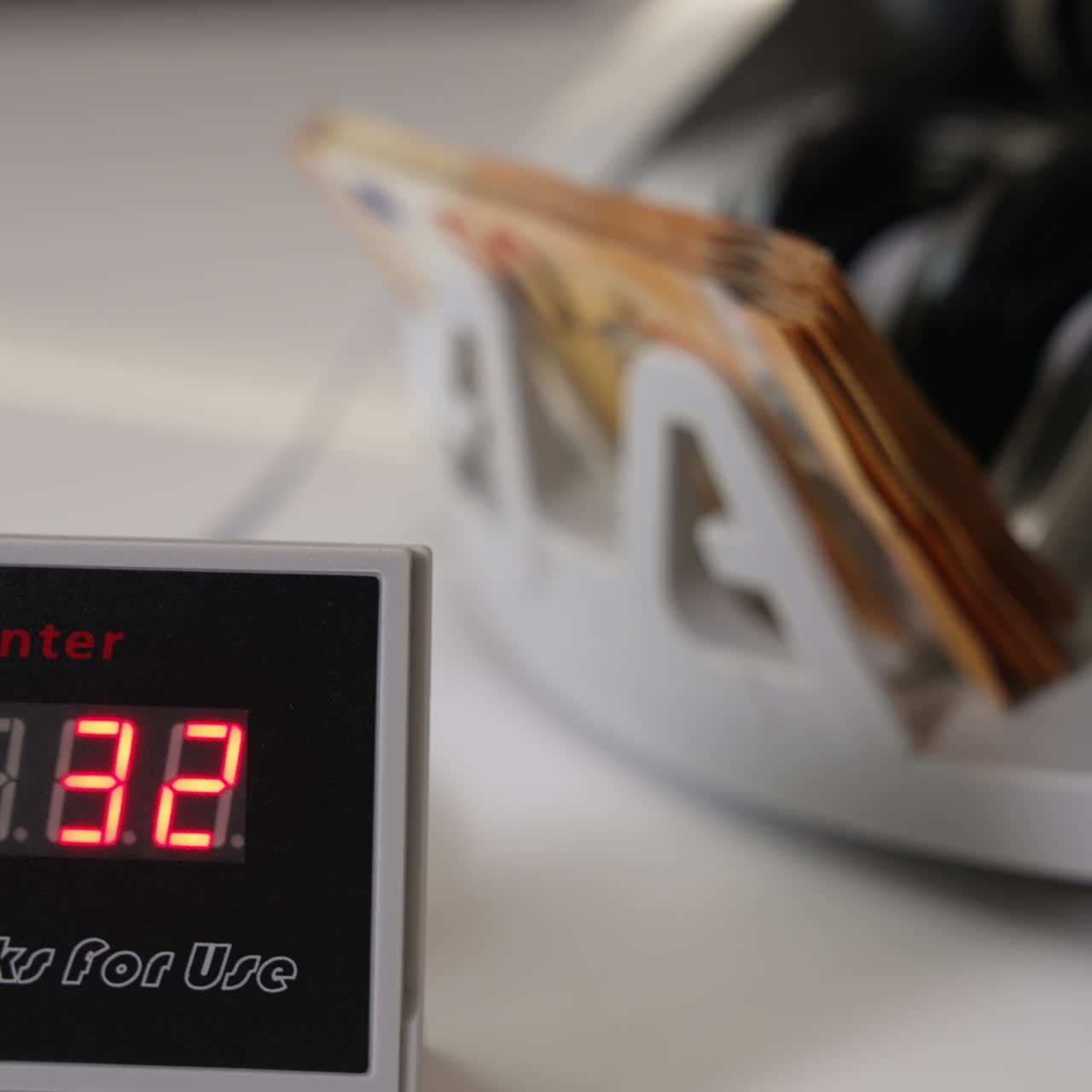 Orange banknotes falling on the holder of money counting machine. Male hand takes a wad of cash from equipment. Little screen showing the number of bills. Close up. Blurred backdrop