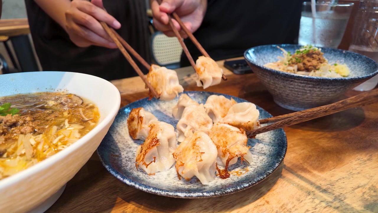 Close-up of people using chopsticks to pick up fried dumplings from a blue plate.