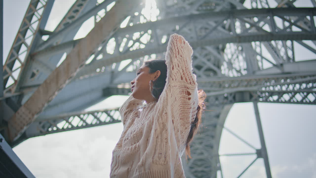Charming girl touching hair posing metal structure at sunny city street closeup