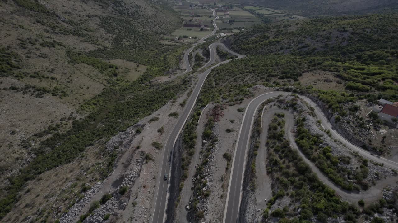 video de drones del plano frontal al comienzo del paso de montaña de la autopista sh20 en bridje albania, al fondo se puede ver el lago skadar, se pueden ver casas de la ciudad, camino sinuoso