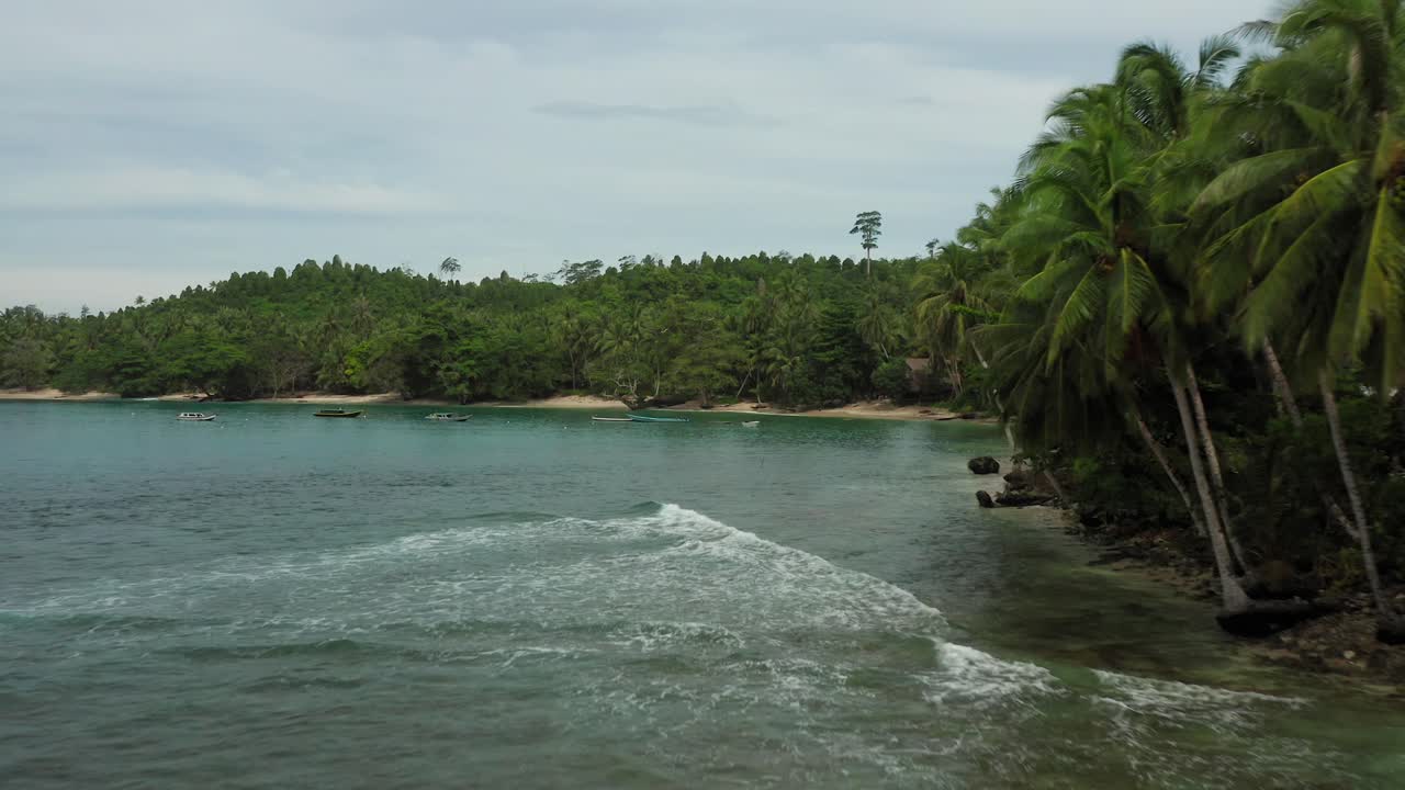 Aerial flight above breaking waves along Indonesian palm jungle waterfront