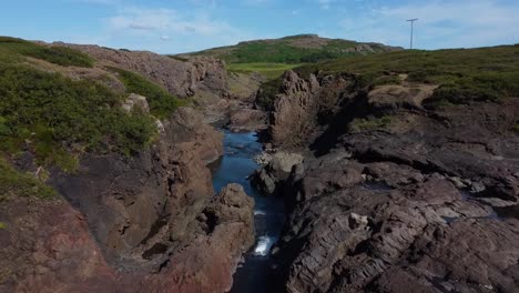 río de sobrevuelo aéreo entre colinas rocosas y montaña verde en el fondo a la luz del sol en islandia