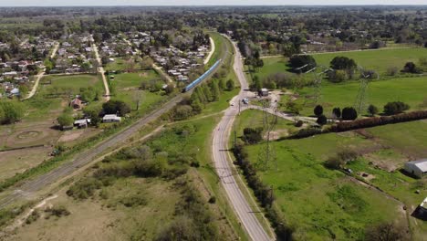 Aerial-shot-of-train-and-cars-driving-between-rural-suburb-area-in-Buenos-Aires-during-sunlight