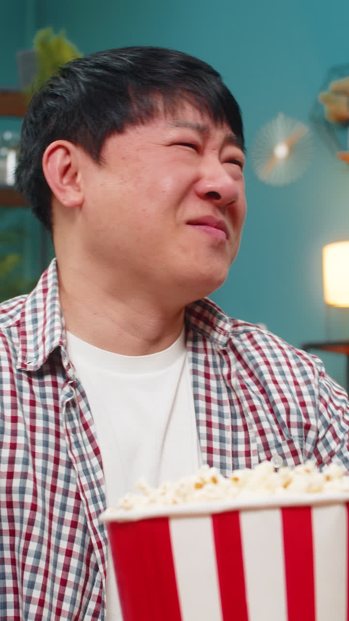 Asian man laughing watching comedy movie holding stomach and eating popcorn joyful relaxing moment
