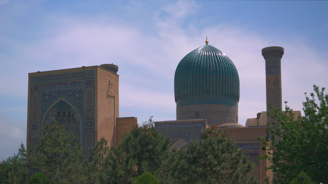 Ampia veduta cinematografica di uno skyline con cupole storiche piastrellate e minareti che si stagliano sopra gli alberi del giardino con facciate a mosaico decorate, cielo azzurro pulito, tranquillo paesaggio urbano con monumenti culturali in silhouette leggibili in 4k