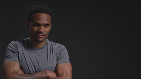 studio portrait of male athlete sport training or exercising in gym folding arms against black background with copy space