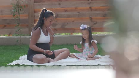 a mother and her young daughter sit on a blanket in the backyard, engaging in a drawing activity together. the outdoor scene captures a peaceful family moment, fostering creativity and bonding.