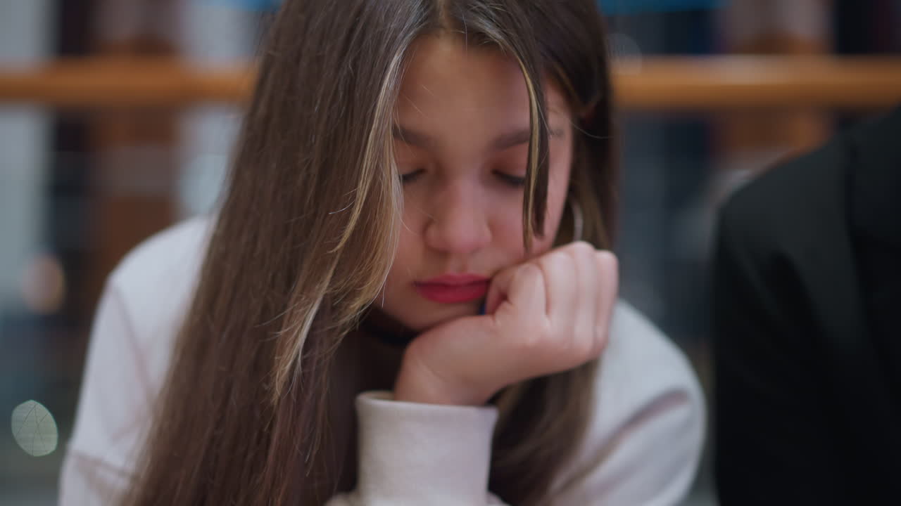Close up of young girl resting hand under jaw while operating phone with red and blue nail paint showing thoughtful expression modern lifestyle youth culture technology use