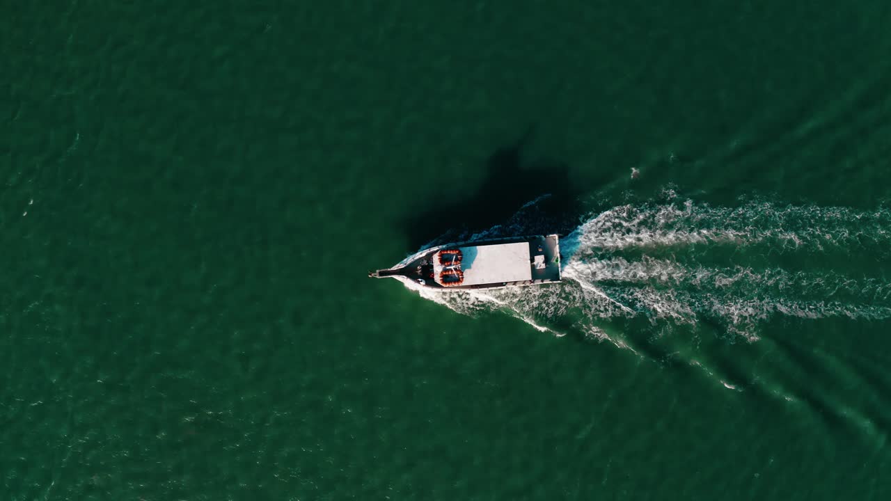 South Padre Island, Texas'ta yeşil açık suyu geçerken arkasında dalgalanmalar oluşturan beyaz balıkçı teknesinin 4K kalitesinde kuşbakışı drone çekimi.