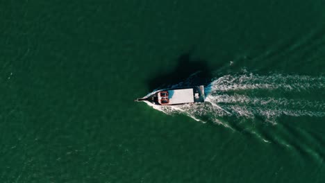 top down aerial drone of white fishing boat crossing green open water with wake rippling behind it in 4k, south padre island texas