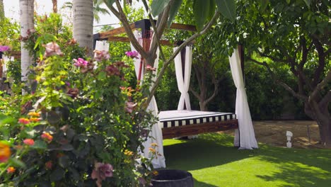 beautiful and luxurious outdoor white four poster bed with white curtains on a wooden set in the backyard of a luxury resort during a sunny summer vacation. trucking shot