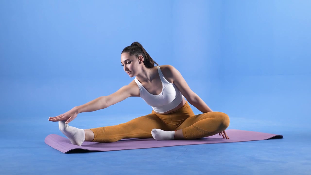Junge Frau macht sitzende Bein-Dehnung auf einer Yogamatte