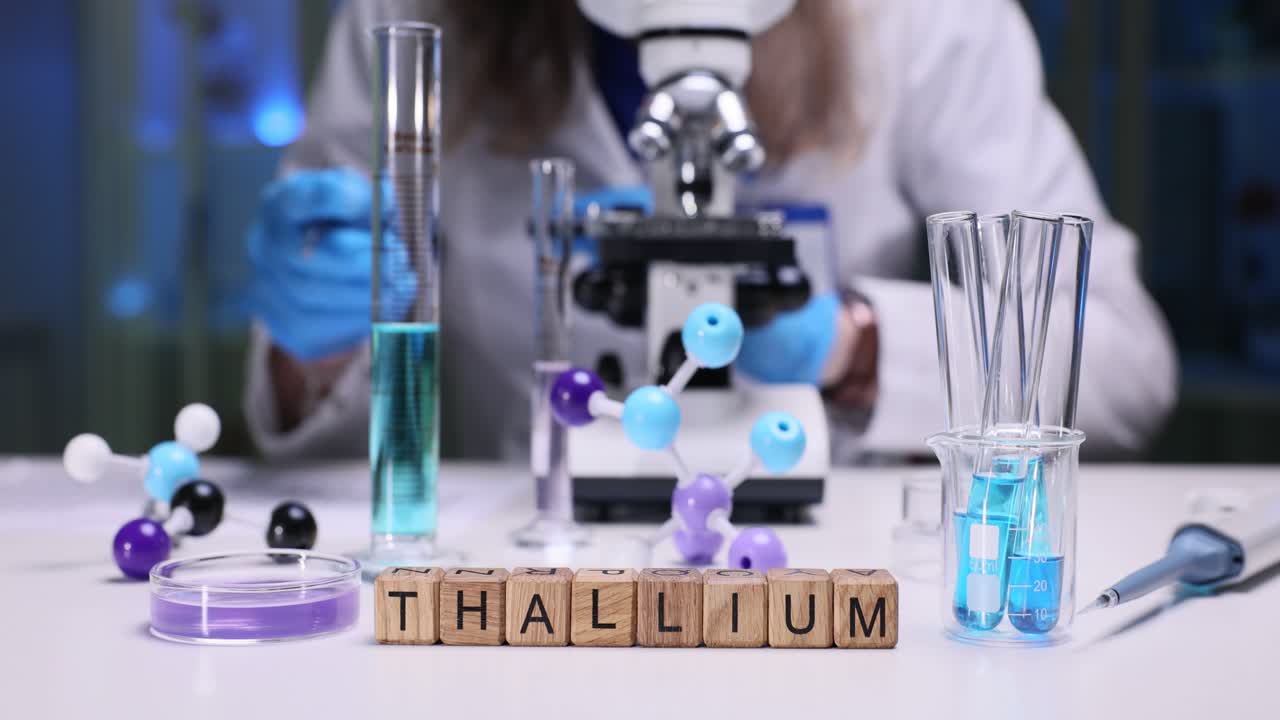 ลูกบาศก์ไม้สะกดคำว่าแทลเลียมบนโต๊ะห้องปฏิบัติการข้างนักวิทยาศาสตร์