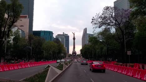 red car drives down reforma avenue toward the angel of independence in mexico city at dusk