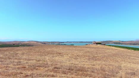 Low-angle-aerial-view-of-dry-crops-with-view-on-lago-poma,-sicily