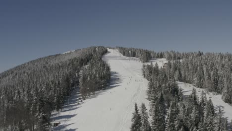 ribnica one track at kope ski resort slovenia with descending skiers and snowboarders, aerial approach shot