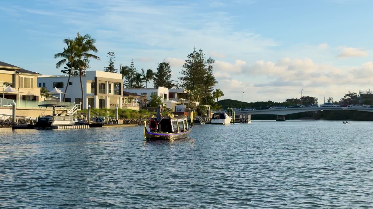 Gondola boat glides past waterfront homes on Nerang River, Gold Coast, under soft evening sunlight