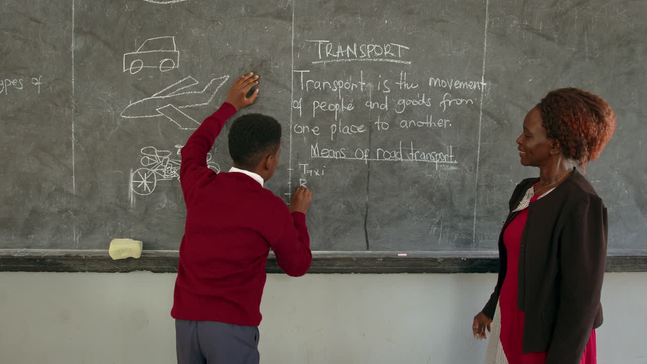 Boy And His Teacher Writing On Blackboard In African School - Medium Shot
